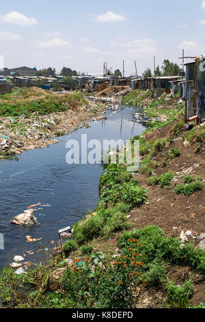 Baraccopoli baracche ed edifici linea il Ngong fiume che è inquinata con rifiuti, rifiuti in plastica e spazzatura, Nairobi, Kenia Foto Stock