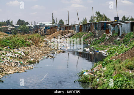 Baraccopoli baracche ed edifici linea il Ngong fiume che è inquinata con rifiuti, rifiuti in plastica e spazzatura, Nairobi, Kenia Foto Stock