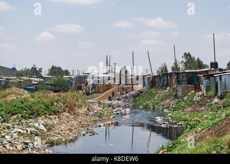 Baraccopoli baracche ed edifici linea il Ngong fiume che è inquinata con rifiuti, rifiuti in plastica e spazzatura, Nairobi, Kenia Foto Stock