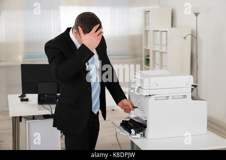 Imprenditore irritata guardando la carta bloccata nella stampante in ufficio Foto Stock