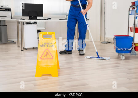 Sezione bassa di bidello maschio piano di pulizia con mop in ufficio Foto Stock