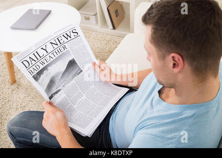 Angolo di alta vista di metà uomo adulto la lettura di notizie meteo sul quotidiano a casa Foto Stock