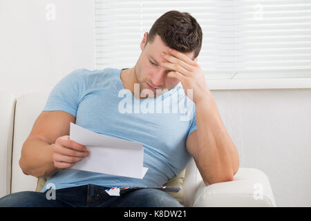 Sconvolto metà uomo adulto con testa in mano la lettera di lettura sul divano di casa Foto Stock