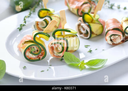 Antipasto di zucchine i rotoli con deliziosi piatti della cucina italiana il prosciutto e il formaggio cremoso con basilico servito su un piatto bianco Foto Stock