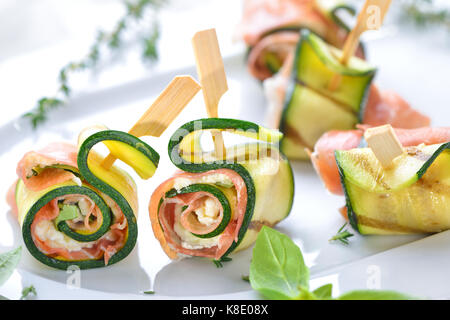 Antipasto di zucchine i rotoli con deliziosi piatti della cucina italiana il prosciutto e il formaggio cremoso con basilico servito su un piatto bianco Foto Stock