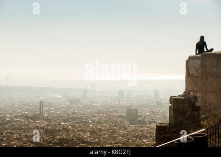 Backlit turista femminile guardando fuori dalla parte superiore della parete a Barcellona cityscape, Spagna Foto Stock