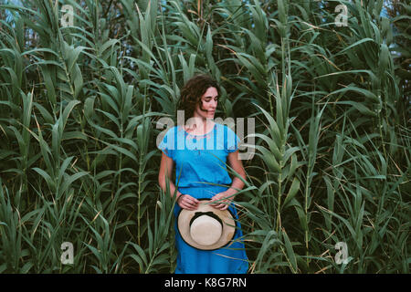 Donna che mantiene hat stando in piedi in mezzo a piante sul campo Foto Stock