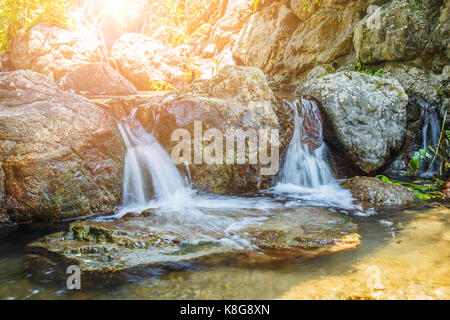 Una piccola cascata nel giardino con la luce del sole. Foto Stock