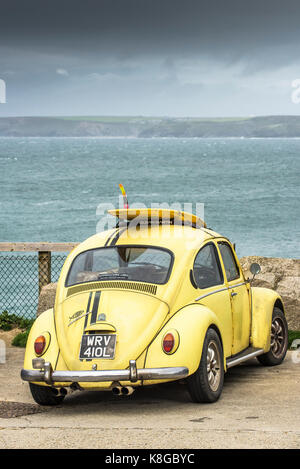 Volkswagen auto - un giallo Volkswagen con una tavola da surf sulla sua portabagagli per tetto parcheggiato a poco Fistral in Newquay, Cornwall Foto Stock