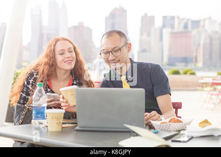 Imprenditore e la donna utilizzando laptop a waterfront cafe tabella, New York, Stati Uniti d'America Foto Stock
