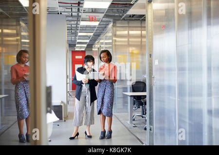 Due imprenditrici nel corridoio di office, guardando a tavoletta digitale Foto Stock