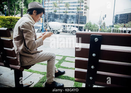 Giovane uomo seduto su un banco di lavoro, utilizza lo smartphone Foto Stock
