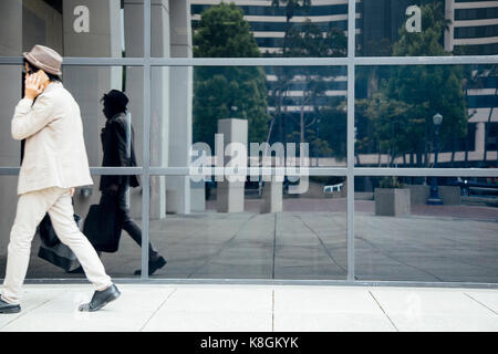 Giovane uomo a camminare lungo edificio per uffici, utilizza lo smartphone Foto Stock