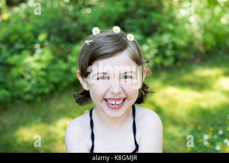 Ritratto di giovane ragazza all'aperto, indossando margherite nei capelli, sorridente Foto Stock