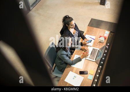 Due imprenditrici seduto alla scrivania, utilizzando laptop, guardando smartphone, vista in elevazione Foto Stock