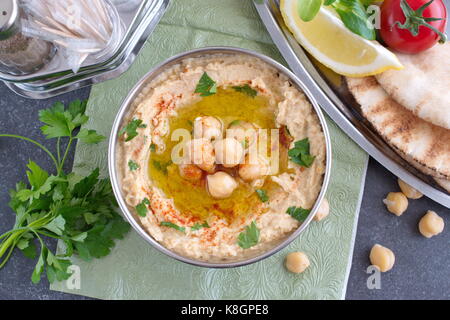 Pasta di ceci con ceci, aglio, cumino, i semi di sesamo, olio di oliva, coriandolo in una ciotola di metallo su un panno verde con pane pita e prezzemolo. Foto Stock