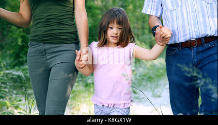 Bellissima bambina con la sindrome di down a piedi con i genitori Foto Stock