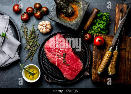 Crudo fresco bistecca di carne il filetto di manzo, erbe aromatiche e spezie intorno al bordo di taglio. Per la cottura di alimenti con sfondo spazio copia. Foto Stock