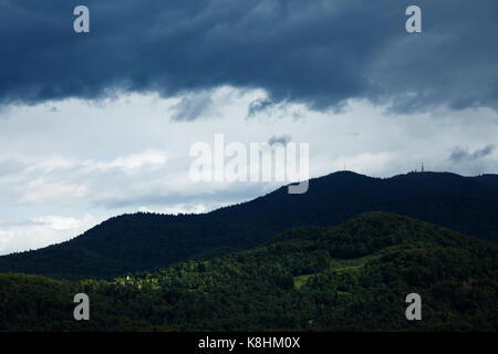 Aria di tempesta su krim montagna, mentre la luce del sole che illumina il villaggio e la chiesa di planinca nelle colline, sul Ljubljansko barje, sout Foto Stock