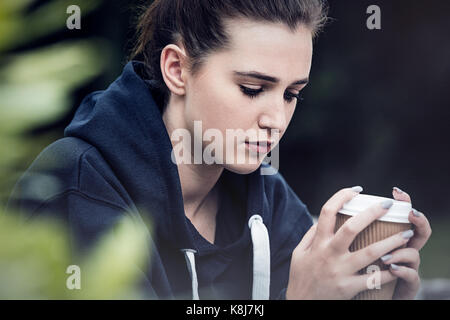 Bella triste premuto ragazza adolescente femmina giovane donna a bere il caffè da asporto al di fuori Foto Stock