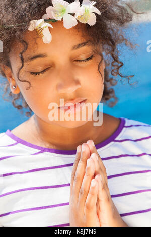 Angelic African American razza mista ragazza bambino gli occhi chiusi in preghiera pregando con fiori nei capelli Foto Stock