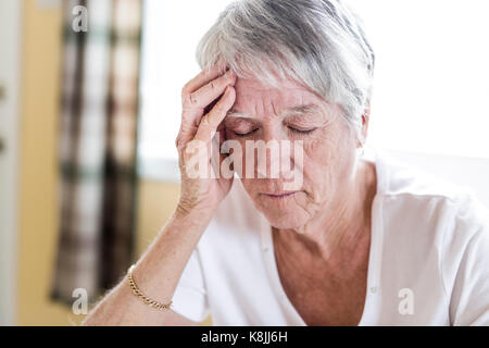 Donna matura a casa toccando la testa con le mani mentre con un mal di testa dolore Foto Stock