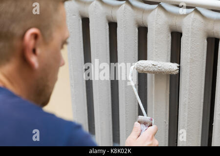 Pittore dipinge il termosifone in ghisa di colore grigio Foto Stock