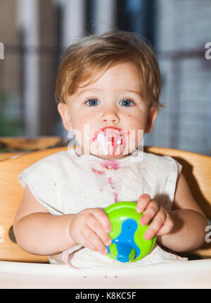 Happy baby disordinato con il cibo sul suo viso dopo aver mangiato il dessert Foto Stock