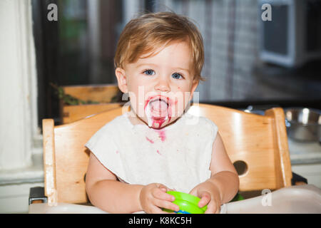 Happy baby disordinato con il cibo sul suo viso dopo aver mangiato il dessert Foto Stock
