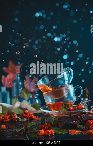 Dark autunno ancora in vita con una coppia di teacups, foglie, frutti di bosco e cannella su un sfondo umido. fotografia d'azione con gocce d'acqua. Foto Stock