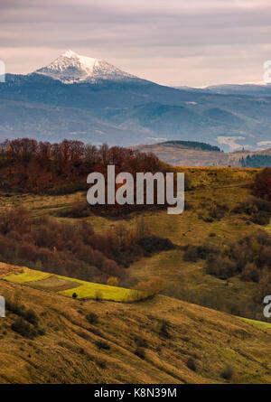 Picco innevato dietro le colline in autunno sotto il cielo nuvoloso Foto Stock