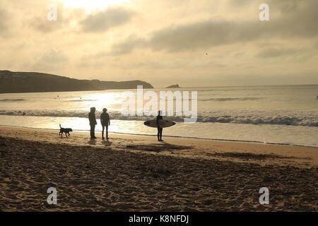 Scena al tramonto di un surfista e cane walkers sulla spiaggia Foto Stock