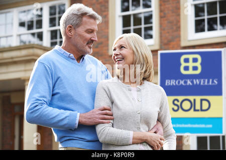 Felice Coppia matura in piedi fuori casa con segno venduti Foto Stock