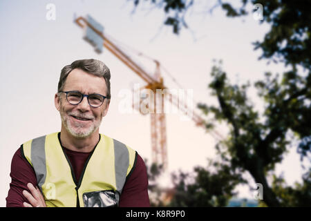 Ritratto di lavoratori anziani wit braccia incrociate indossando abiti riflettenti contro la vista di una gru Foto Stock