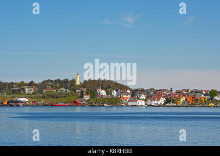 Riva dell'isola di Buøy con una famosa torre d'acqua gialla su una montagna, tradizionali case in legno dipinto e attività portuale industriale Foto Stock