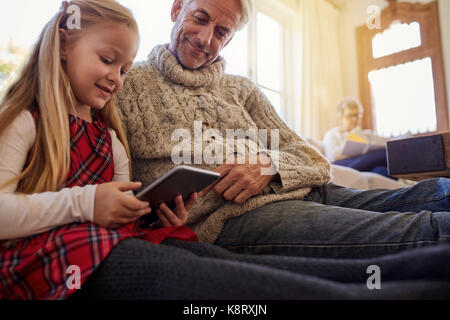 Bambina con il nonno seduti a casa e con tavoletta digitale. Sia la seduta sul pavimento nel soggiorno e guardando il tablet pc con la nonna Foto Stock