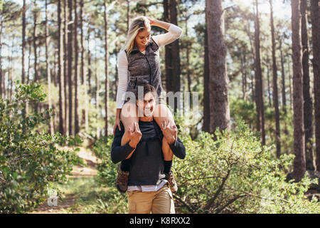 Escursionismo coppia avendo divertimento mentre trekking nella foresta. Equitazione donna piggyback sull'uomo durante le escursioni nella foresta. Foto Stock