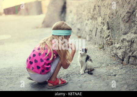 La bionda bambina gioca con un gattino in strada Foto Stock