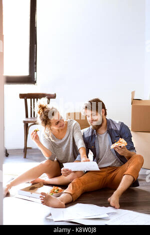 Coppia giovane muovendo nella nuova casa, mangiare la pizza. Foto Stock