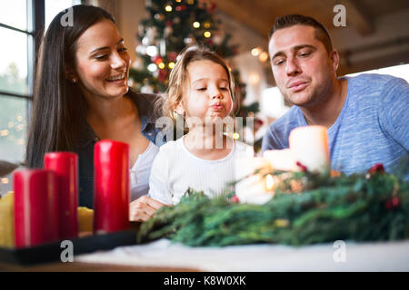 Famiglia giovane soffiando candele sulla corona di Avvento. Foto Stock