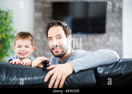 Padre e figli sul divano a casa a guardare la tv insieme Foto Stock