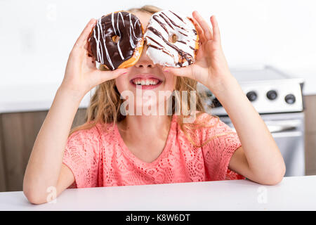 Bambini che giocano con le ciambelle nelle sue mani di metterli sul suo viso Foto Stock