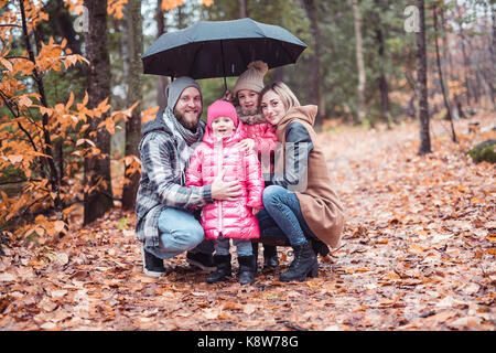 Famiglia sotto ombrellone in autunno il parco cittadino, famiglia felice Foto Stock