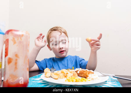 Un giovane ragazzo caucasico seduti a un tavolo a mangiare la sua cena con il ketchup bottiglia in primo piano Foto Stock