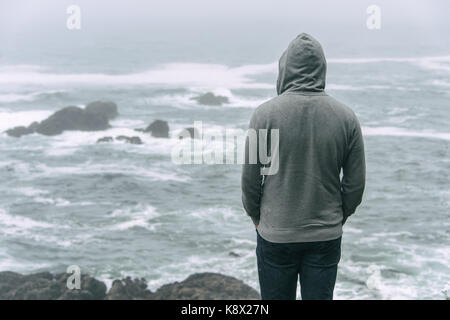 Triste e lonely man standing di fronte all'oceano pacifico e guardando il mare tempestoso sull'isola di Vancouver. Foto Stock