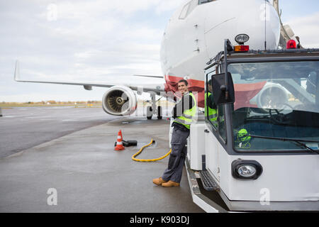 Lavoratore appoggiata sul carrello di traino con aereo in background Foto Stock