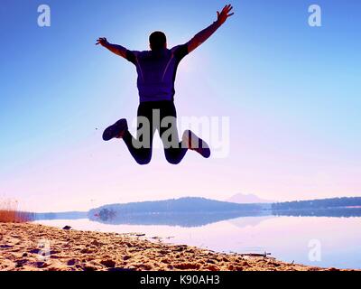 Uomo pazzo salto sulla spiaggia. sportsman battenti sulla spiaggia durante l'incredibile sunrise oltre l'orizzonte Foto Stock