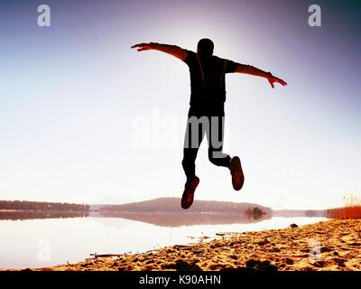 Uomo pazzo salto sulla spiaggia. sportsman battenti sulla spiaggia durante l'incredibile sunrise oltre l'orizzonte Foto Stock