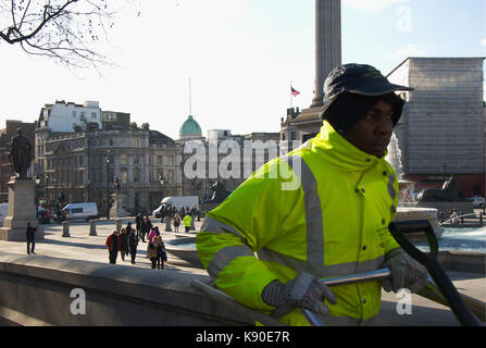 Un pulitore di via passeggiate fino il marciapiede attorno a Trafalgar Square. Foto Stock