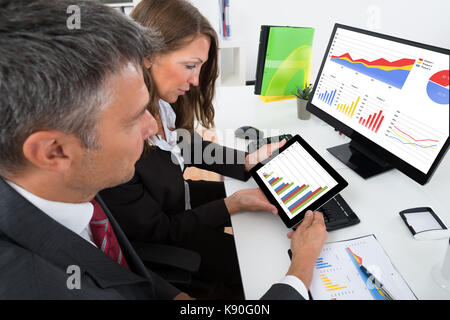 Due imprenditori analizzando il grafico su tavoletta digitale in ufficio Foto Stock